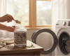 Person measuring laundry detergent into a jar in a laundry room with washing machines.